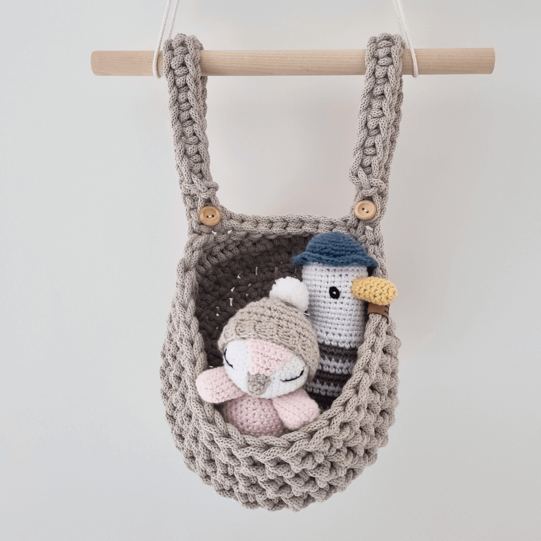 An adorable handmade cot basket is filled with cuddly toys hanging from a wooden dowel.