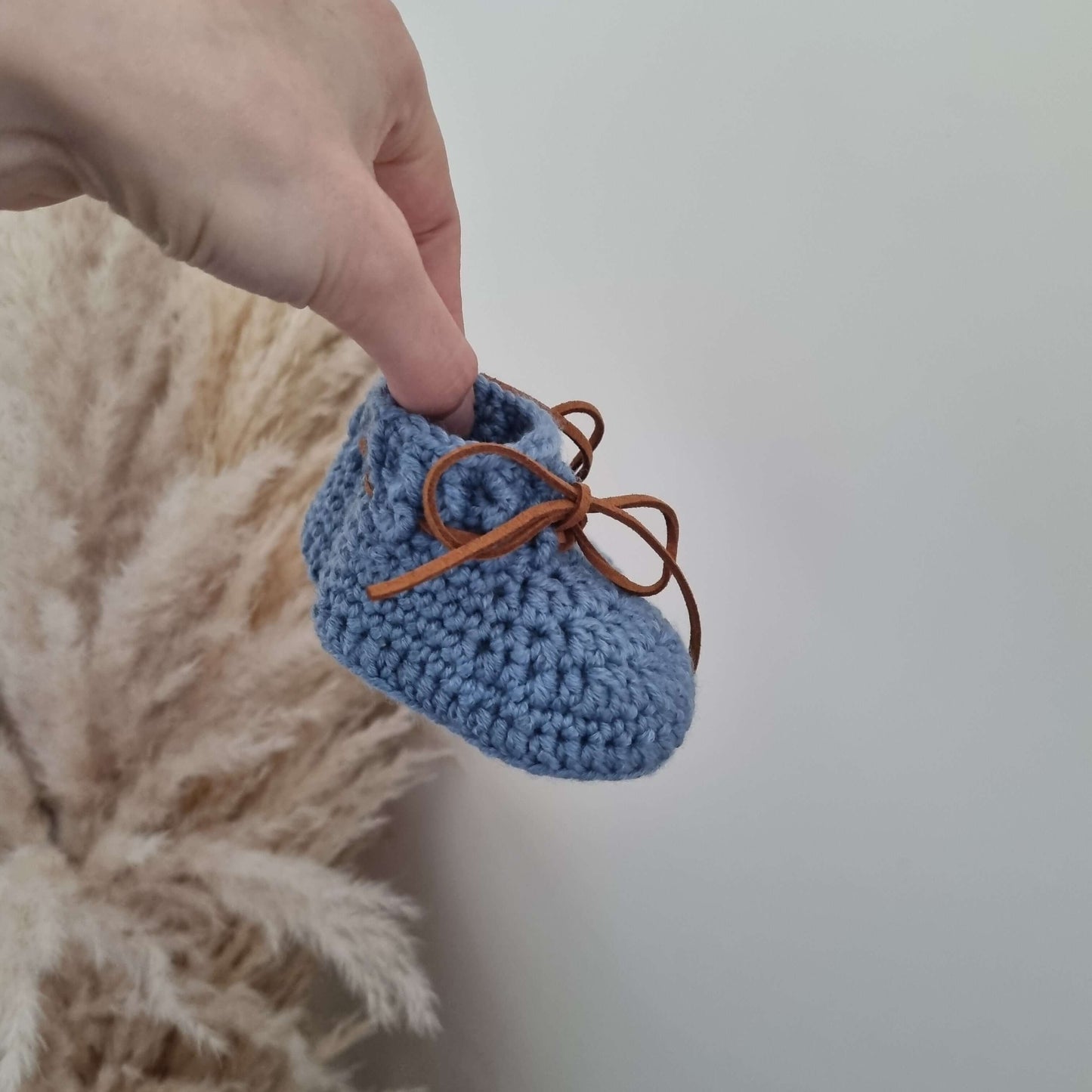 A hand showcases adorable blue baby booties crocheted from cozy Merino wool
