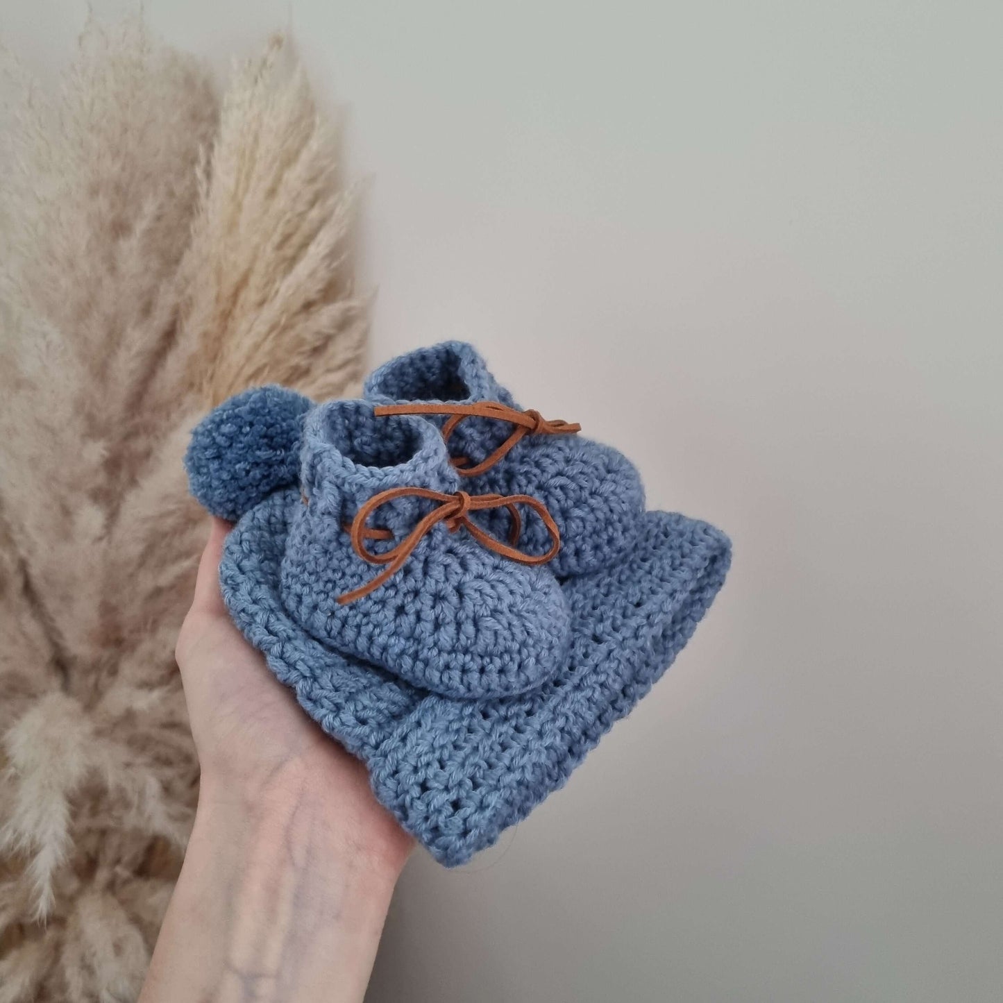 A hand presents a lovely blue baby hat with a matching pair of baby booties, beautifully crocheted from Merino wool.
