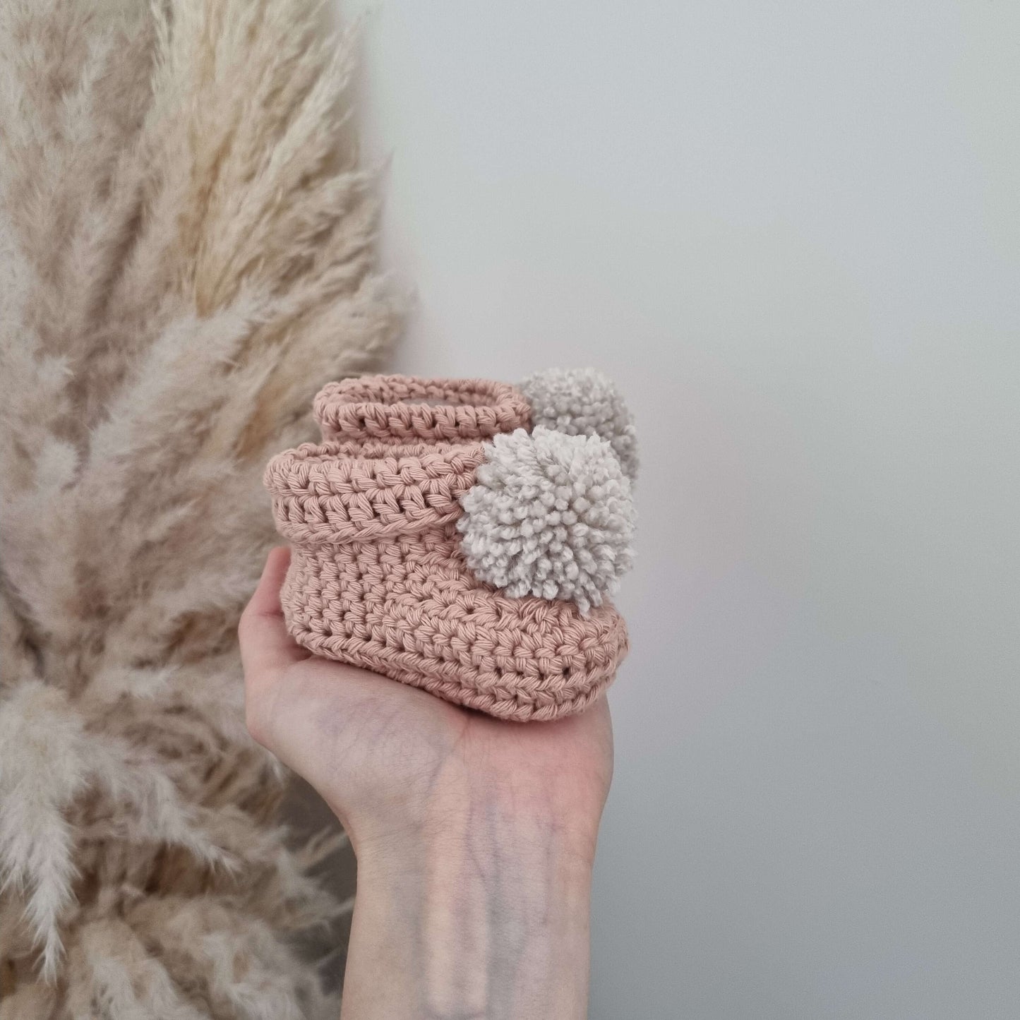 A hand displays adorable clay crocheted baby booties, highlighting their intricate design and cozy appeal for little feet.
