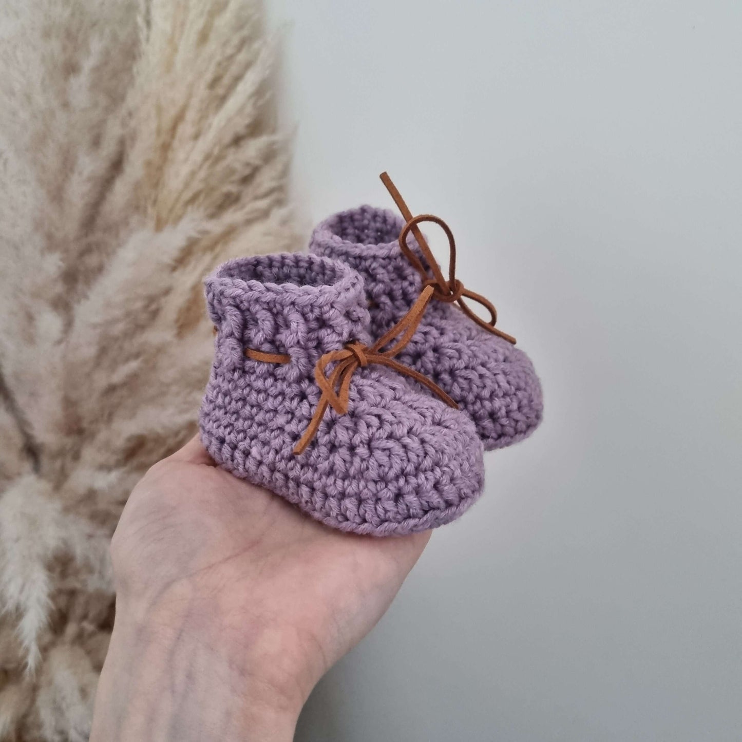 A hand showcases adorable purple baby booties crocheted from cozy Merino wool