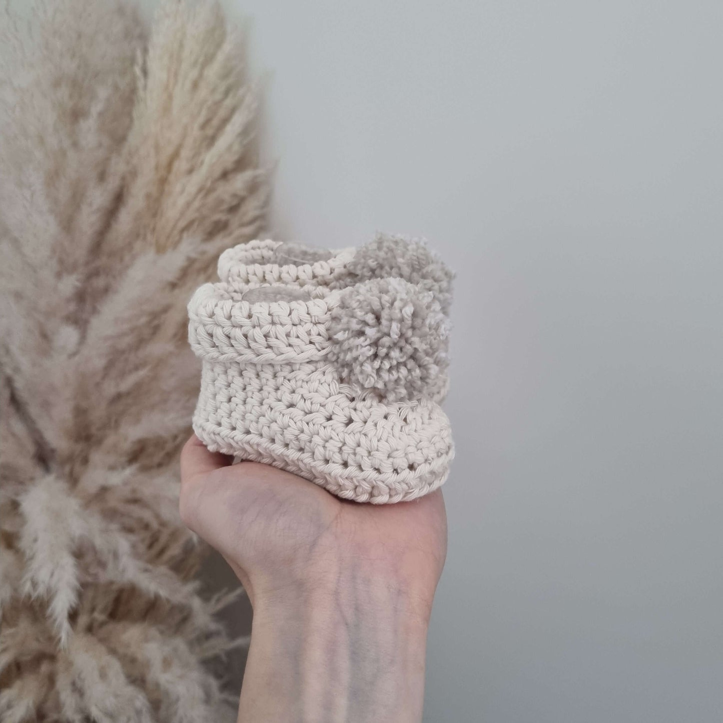 A hand displays charming cream crocheted baby bootie, highlighting its delicate craftsmanship and cozy appeal.