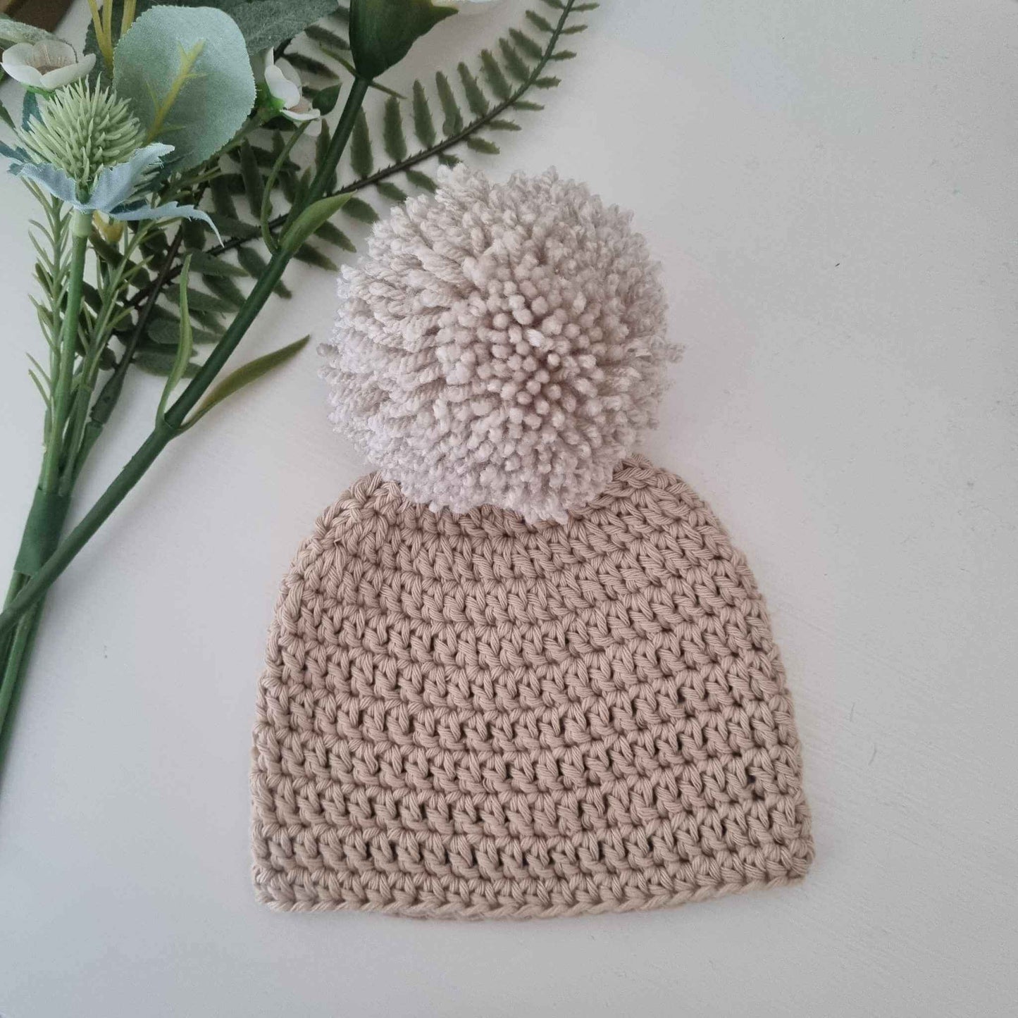 A lovely stone crochet hat topped with a fluffy pom pom, combining warmth and style for the perfect winter accessory.