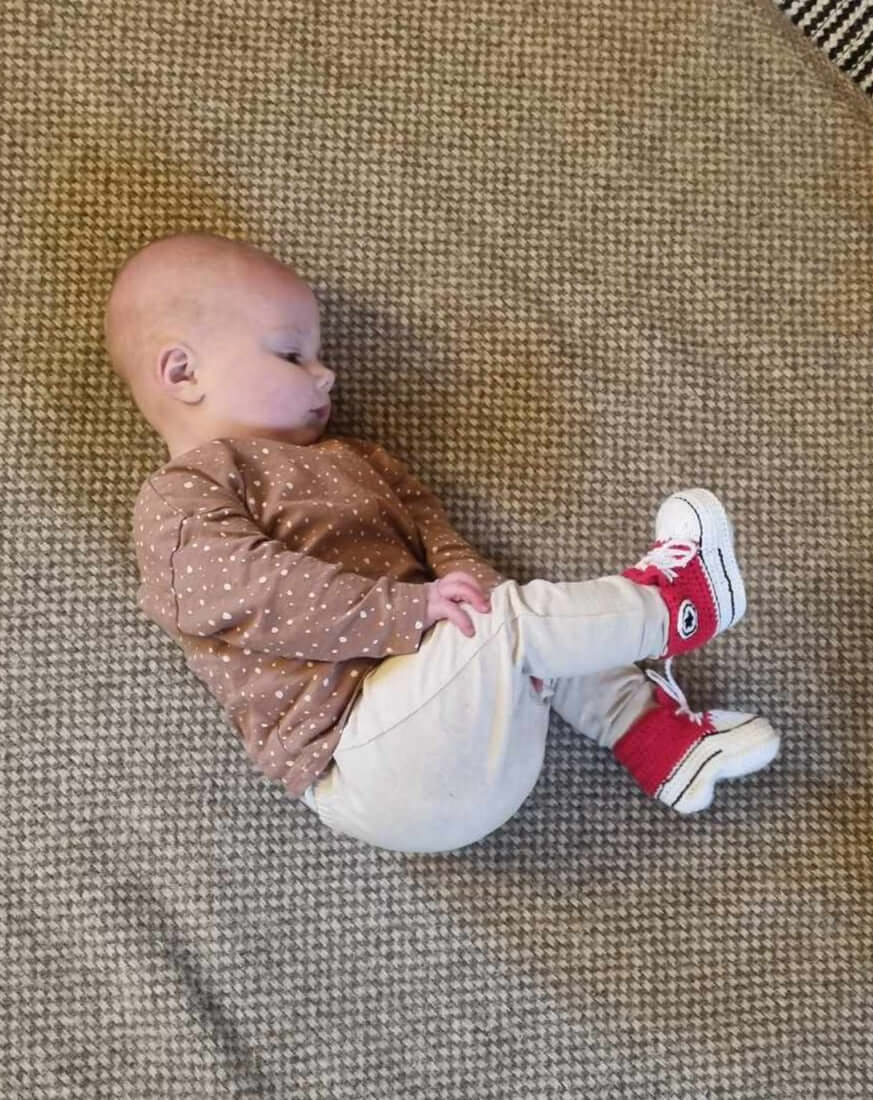 A baby lying on the floor, happily wearing adorable red crochet sneakers.