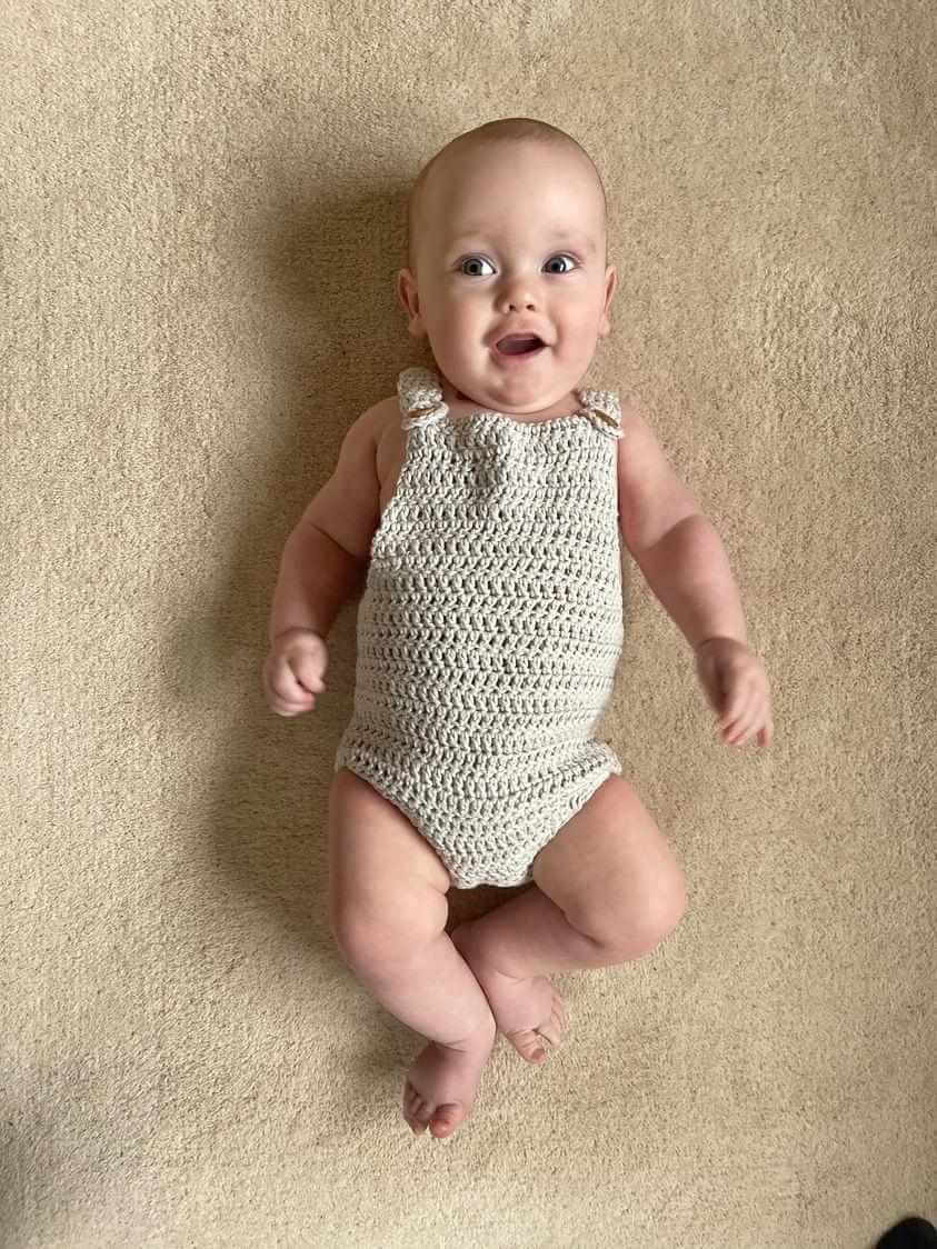 A cute crochet baby romper featuring neutral tones, ideal for keeping your little one cozy and fashionable.