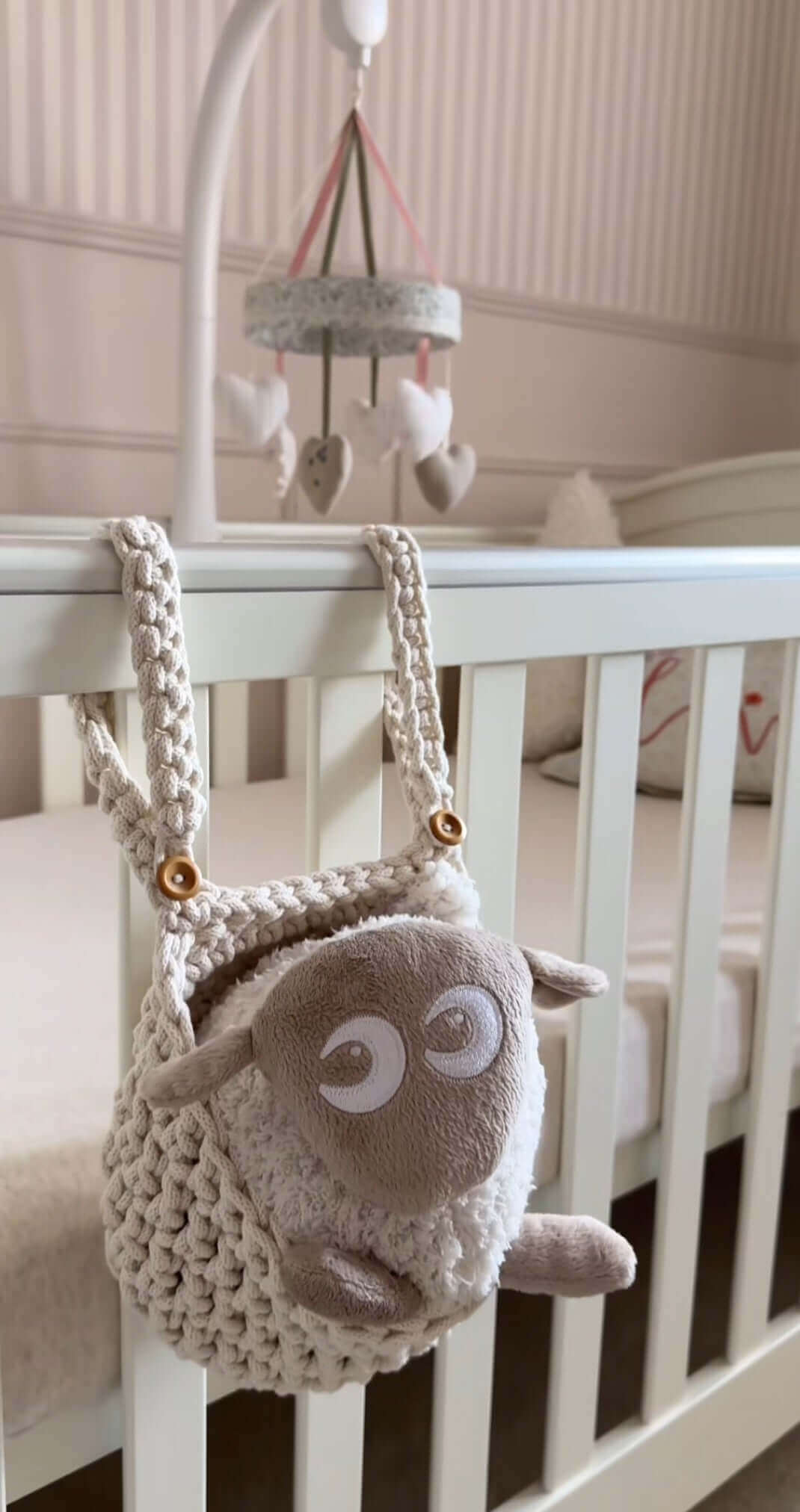 A delightful teddy bear dangles from a handmade cot basket, bringing warmth and joy to the nursery setting.