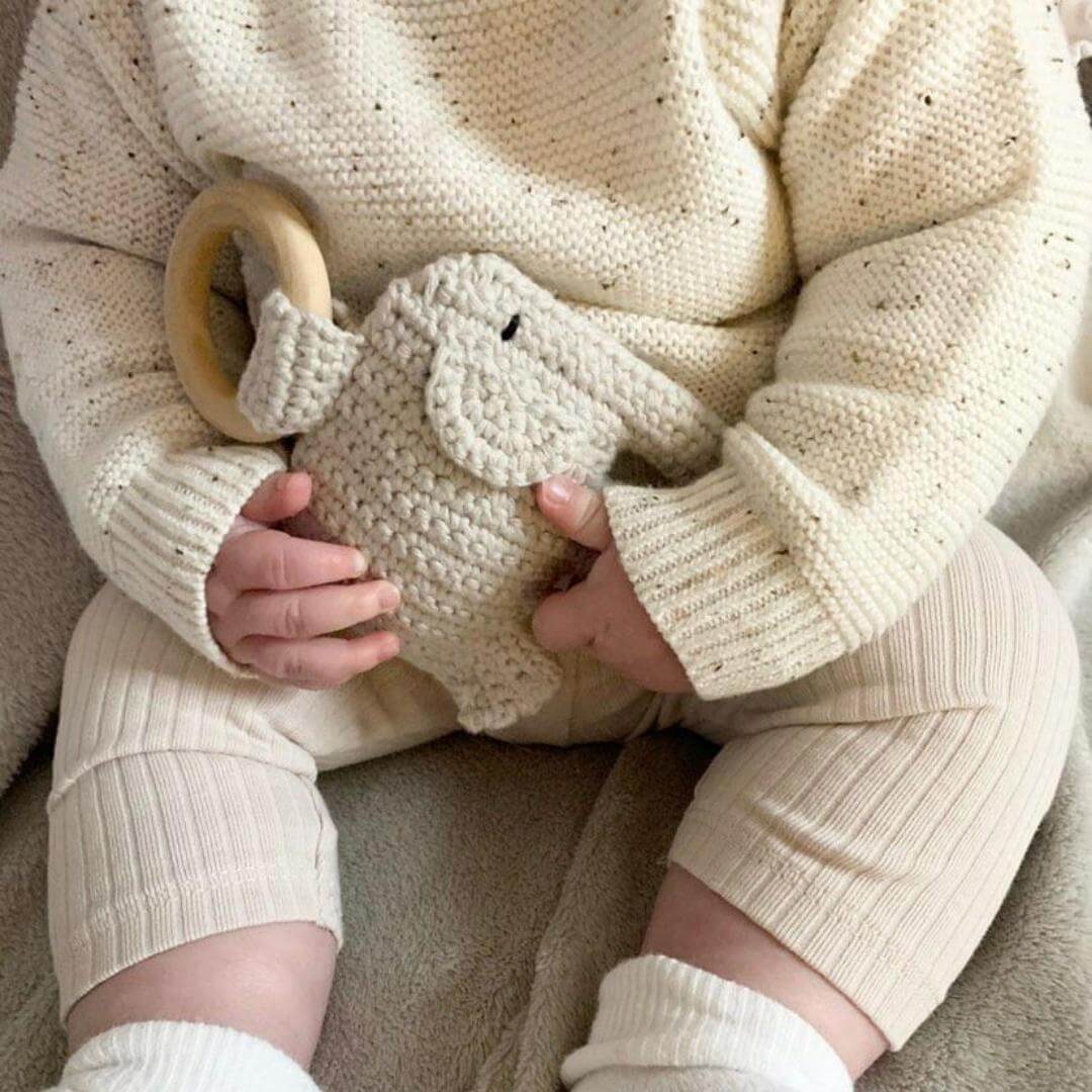 A cute baby in a cozy sweater, happily holding a soft stuffed elephant rattle, radiating warmth and innocence.