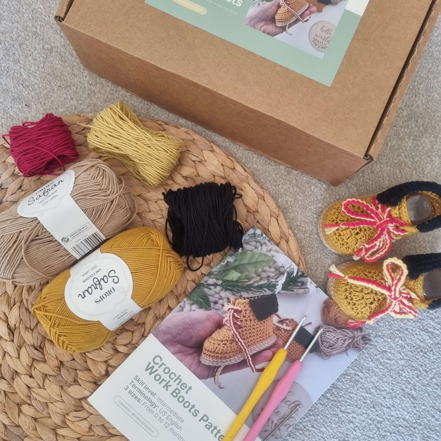 A DIY crochet kit for baby boots displayed, including crochet hooks, yarn in various colors, a sewing needle, and a printed pattern booklet.