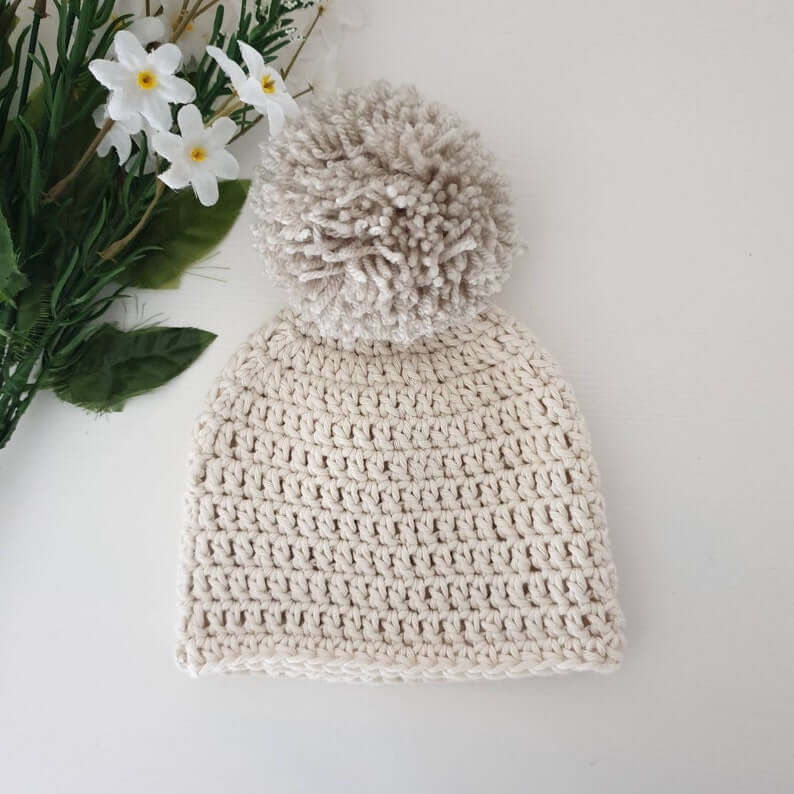 A stylish cream crochet hat with a cute pom pom on top, perfect for chilly days and adding flair to your look.