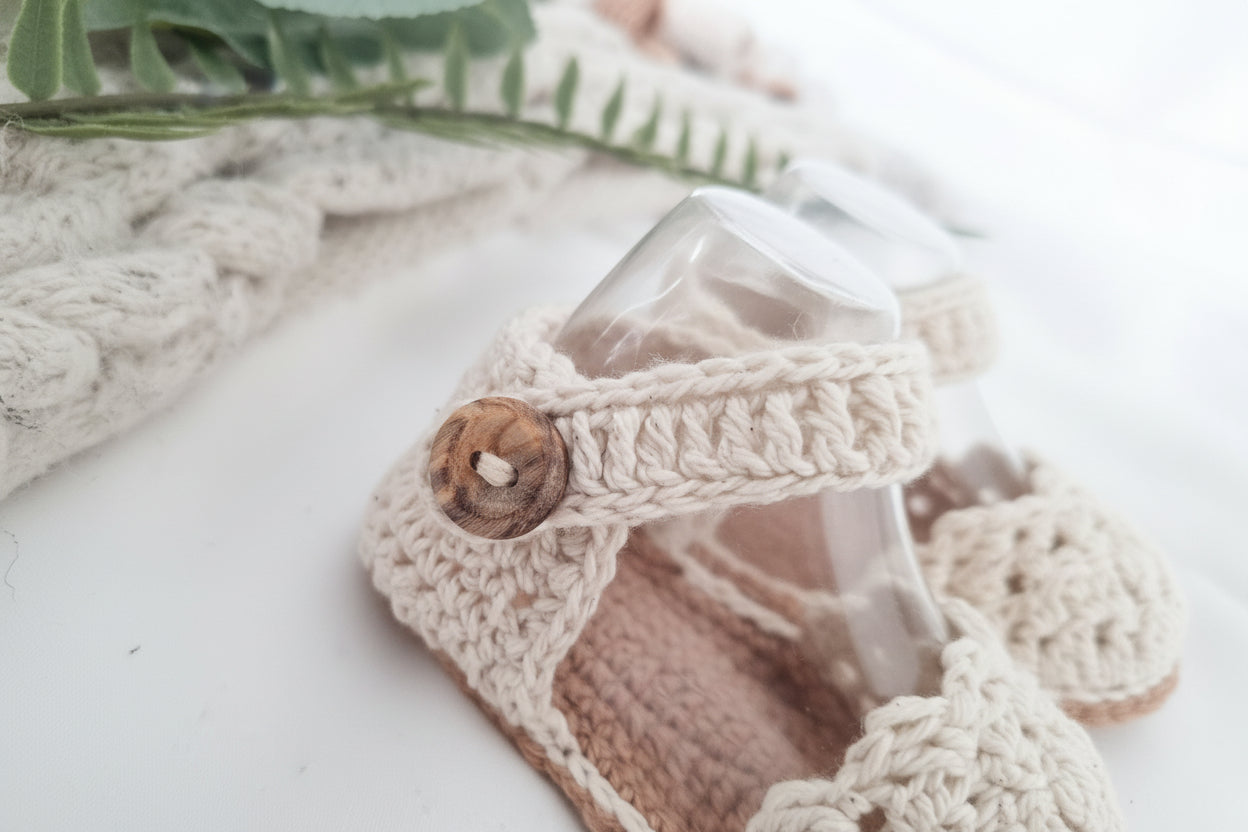 Close-up of a crochet baby sandal with a button on a neutral background