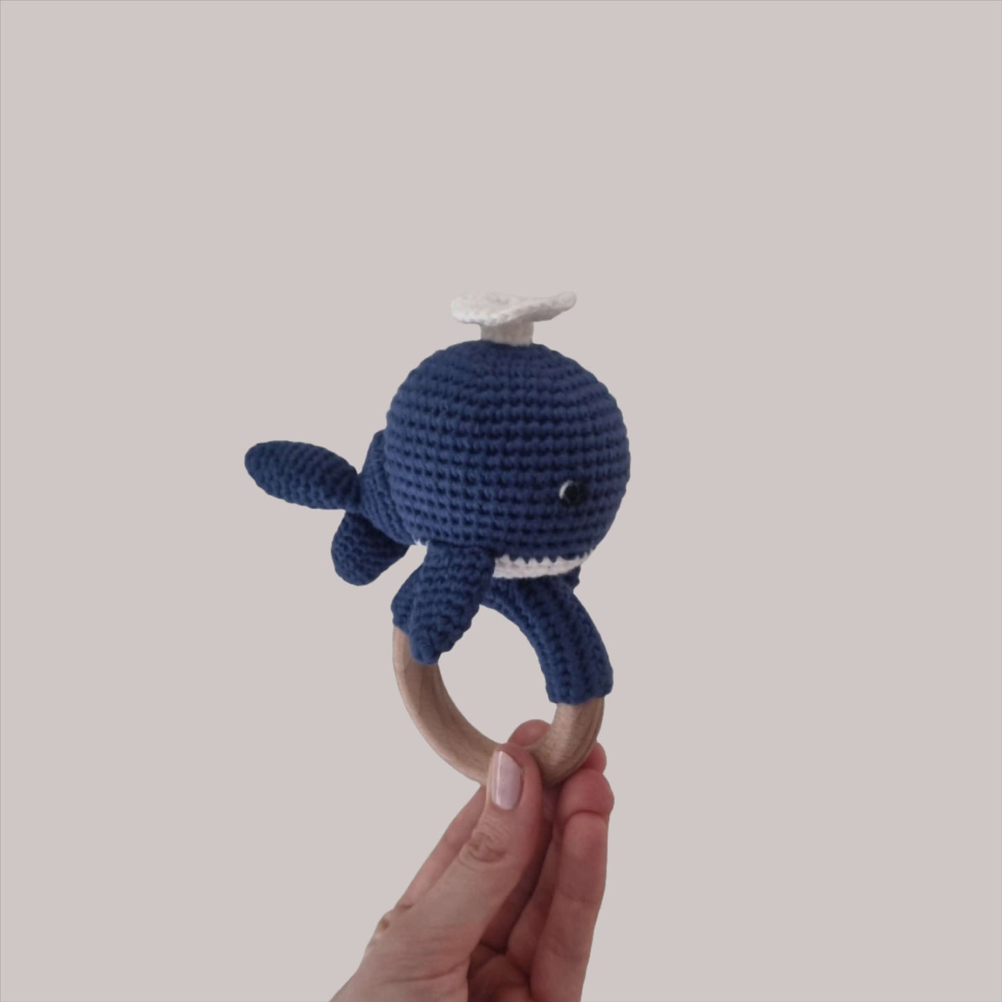 A hand presents a charming crocheted whale rattle, highlighting its adorable features and handmade quality.