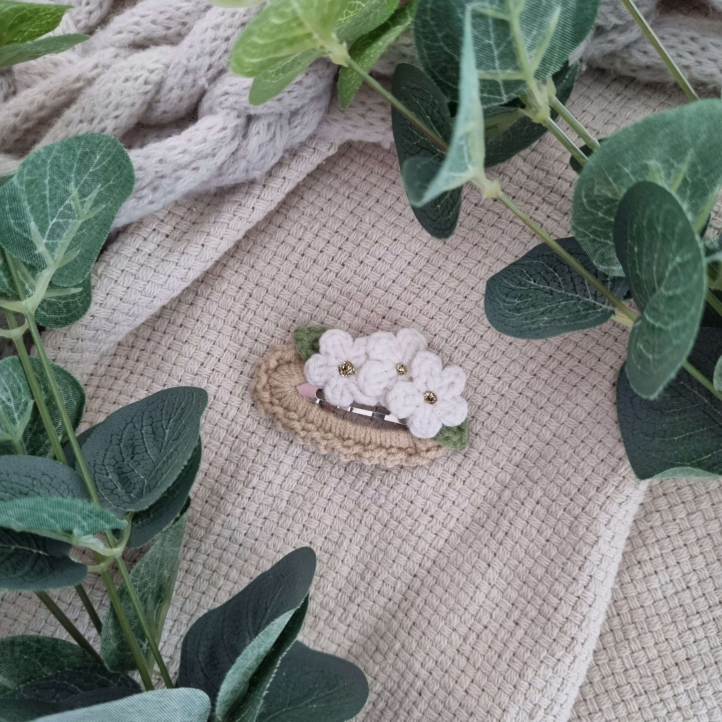 Crochet Flower Hair Clips displayed among soft leaves on a textured fabric background, showcasing handmade design and neutral colors.