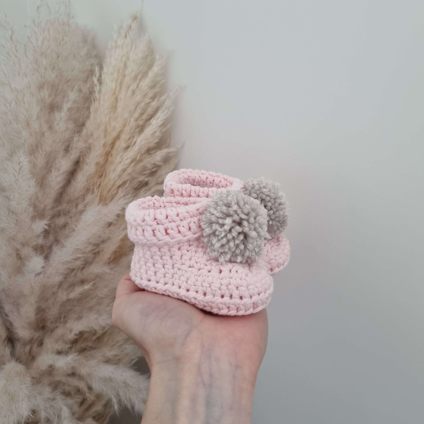 A hand showcases pink crocheted baby bootie, capturing the essence of handmade comfort and creativity.