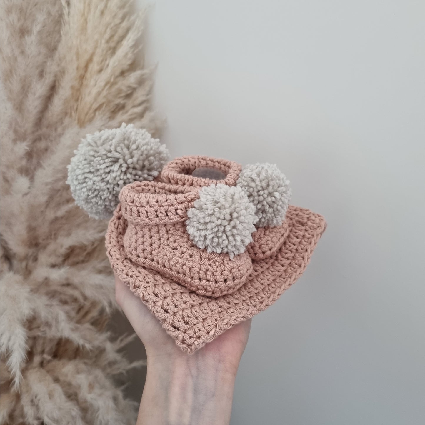 A hand showcases a lovely crocheted hat and two soft pom poms booties, perfect for keeping warm and stylish in winter.