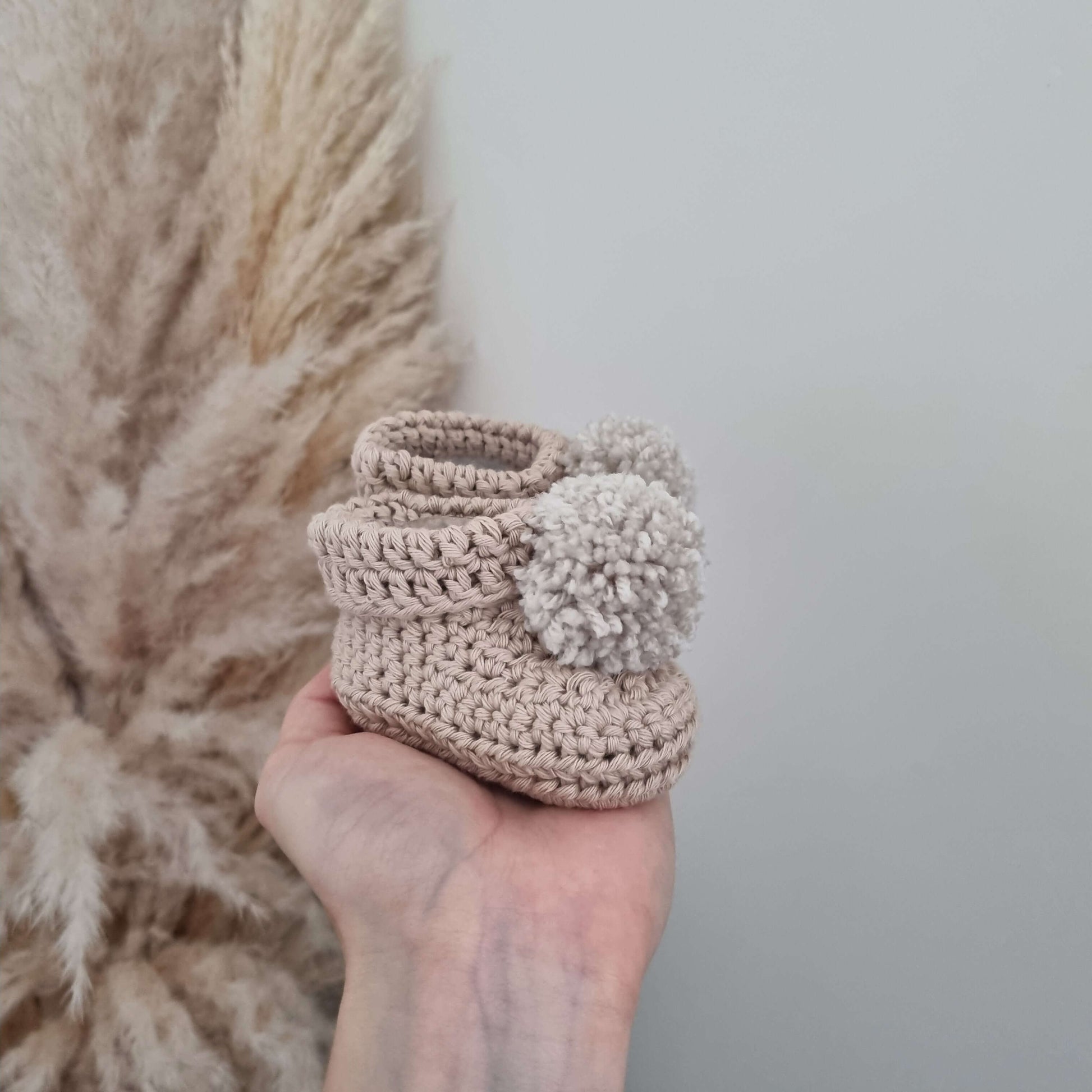 A hand presents charming stone crocheted baby booties, emphasizing their handmade quality and perfect fit for infants.