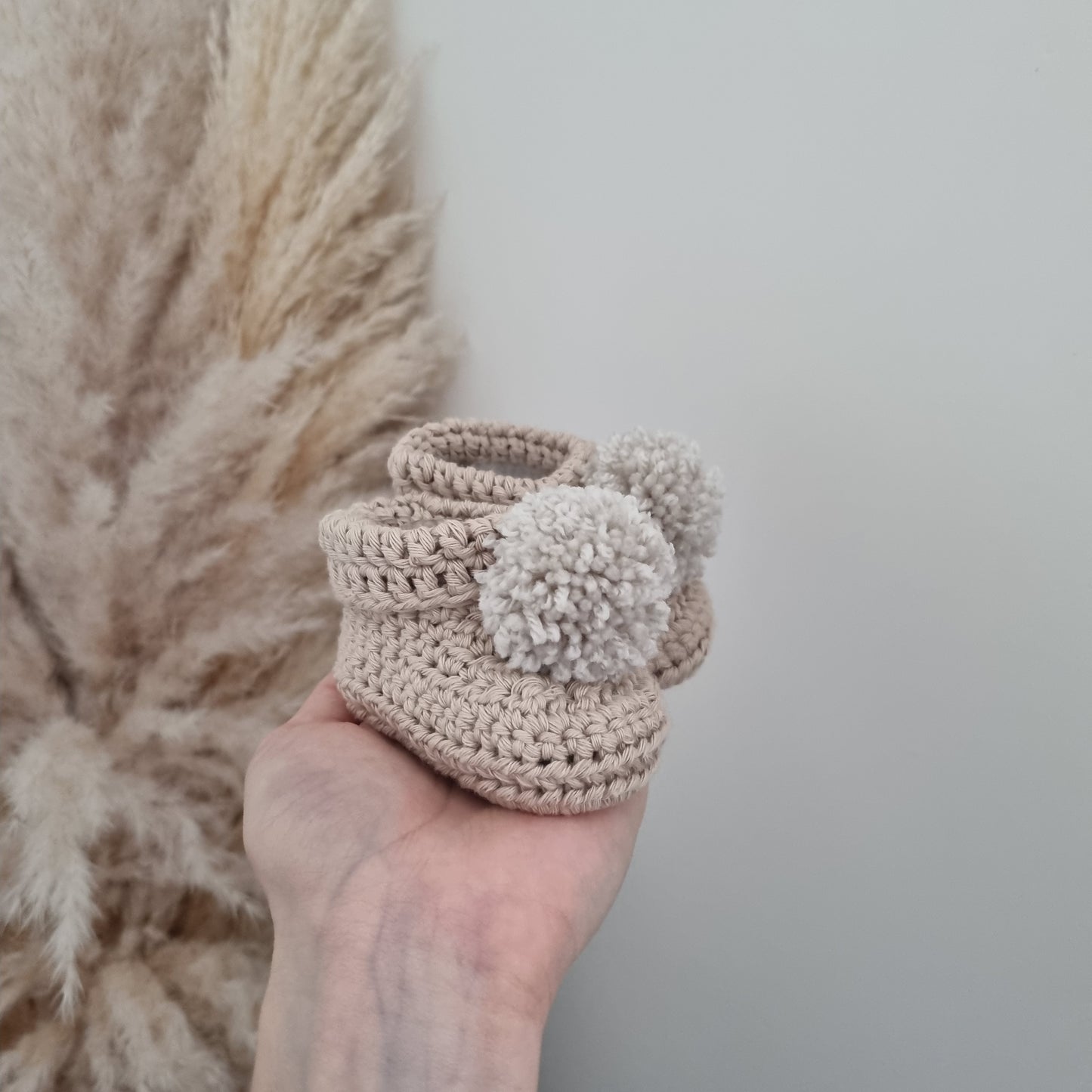 A hand presents charming stone crocheted baby booties, emphasizing their handmade quality and perfect fit for infants.