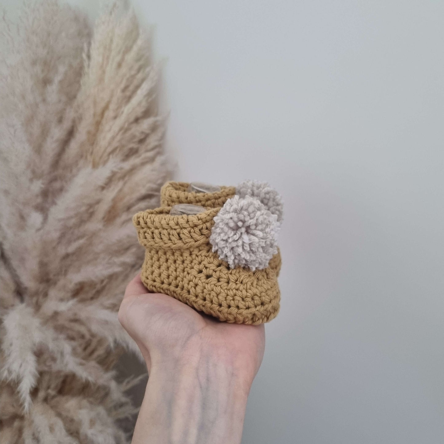 A hand gently hold some mustard crocheted baby booties, showcasing its intricate design and soft texture.