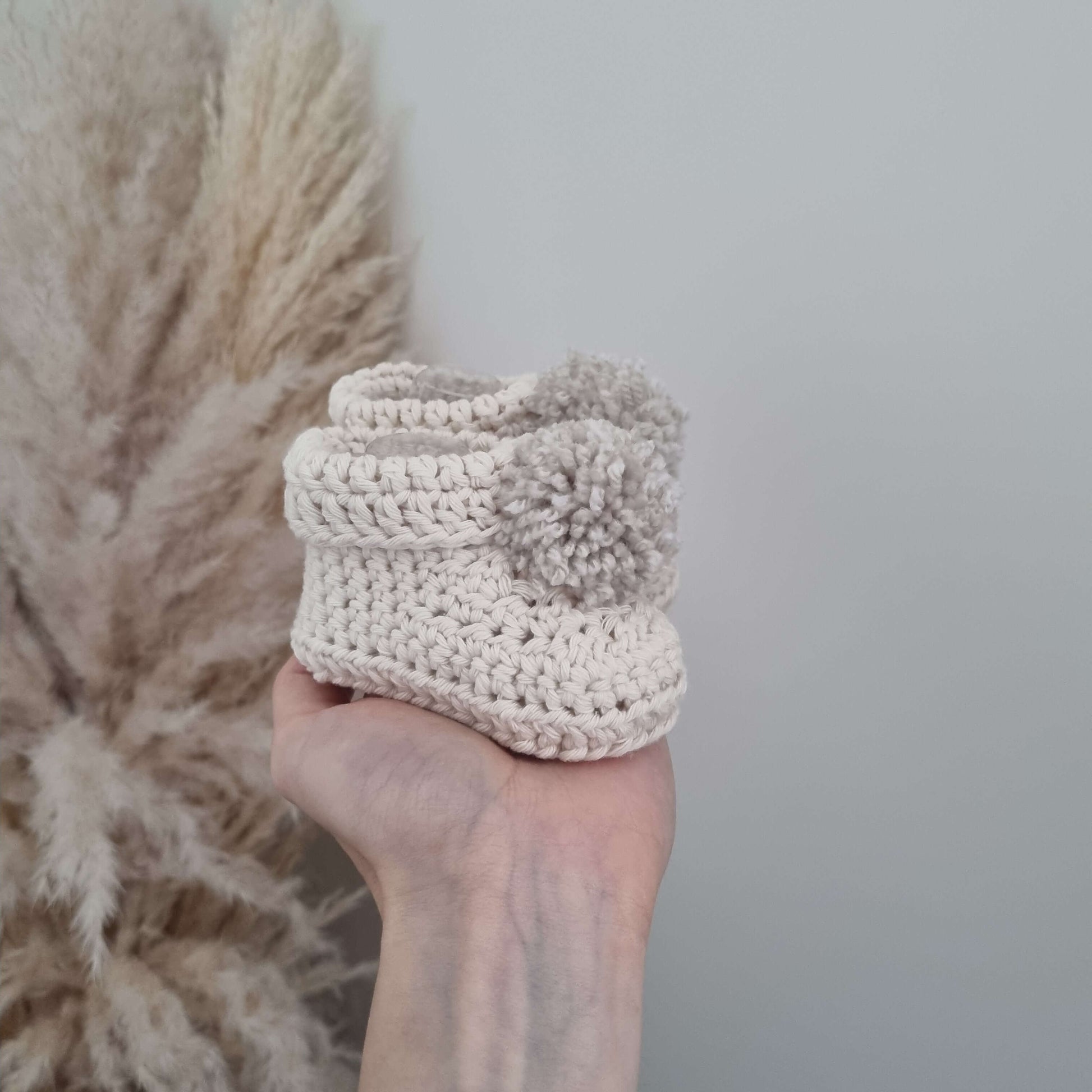  A hand displays charming cream crocheted baby bootie, highlighting its delicate craftsmanship and cozy appeal.