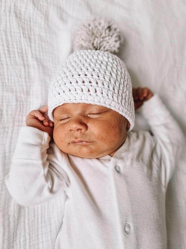 A newborn boy wearing a cozy white crocheted hat, looking adorable and peaceful in his early days of life.