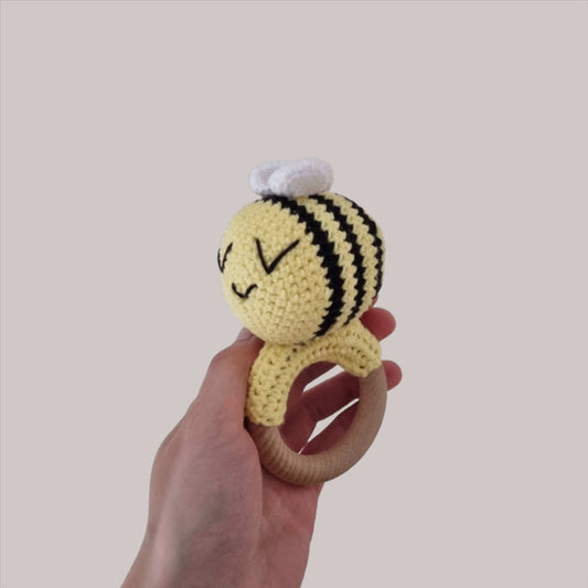 A hand holds a soft, crocheted bumble bee rattle, showcasing its cute design and vibrant colours.