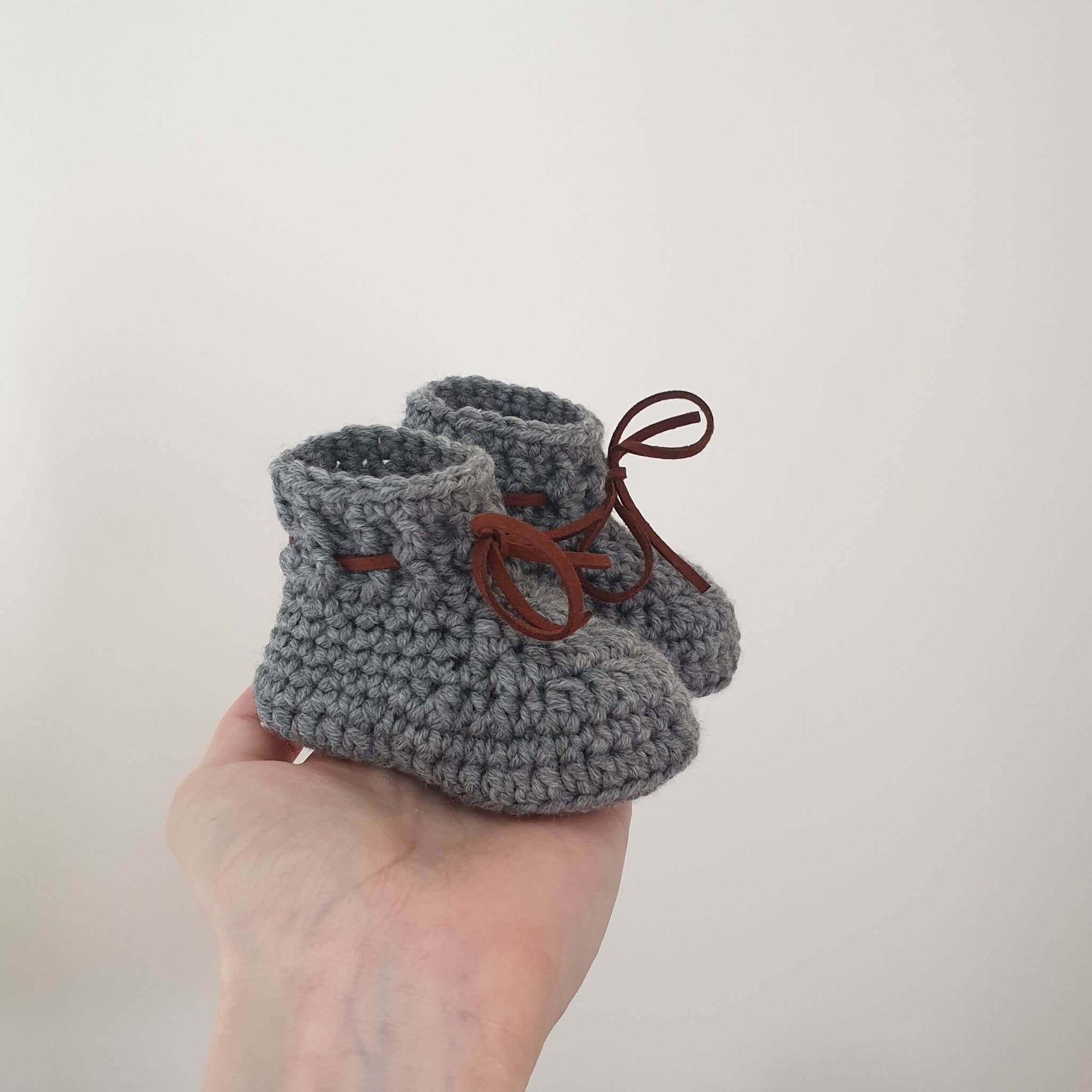 A hand showcases adorable grey baby booties crocheted from cozy Merino wool