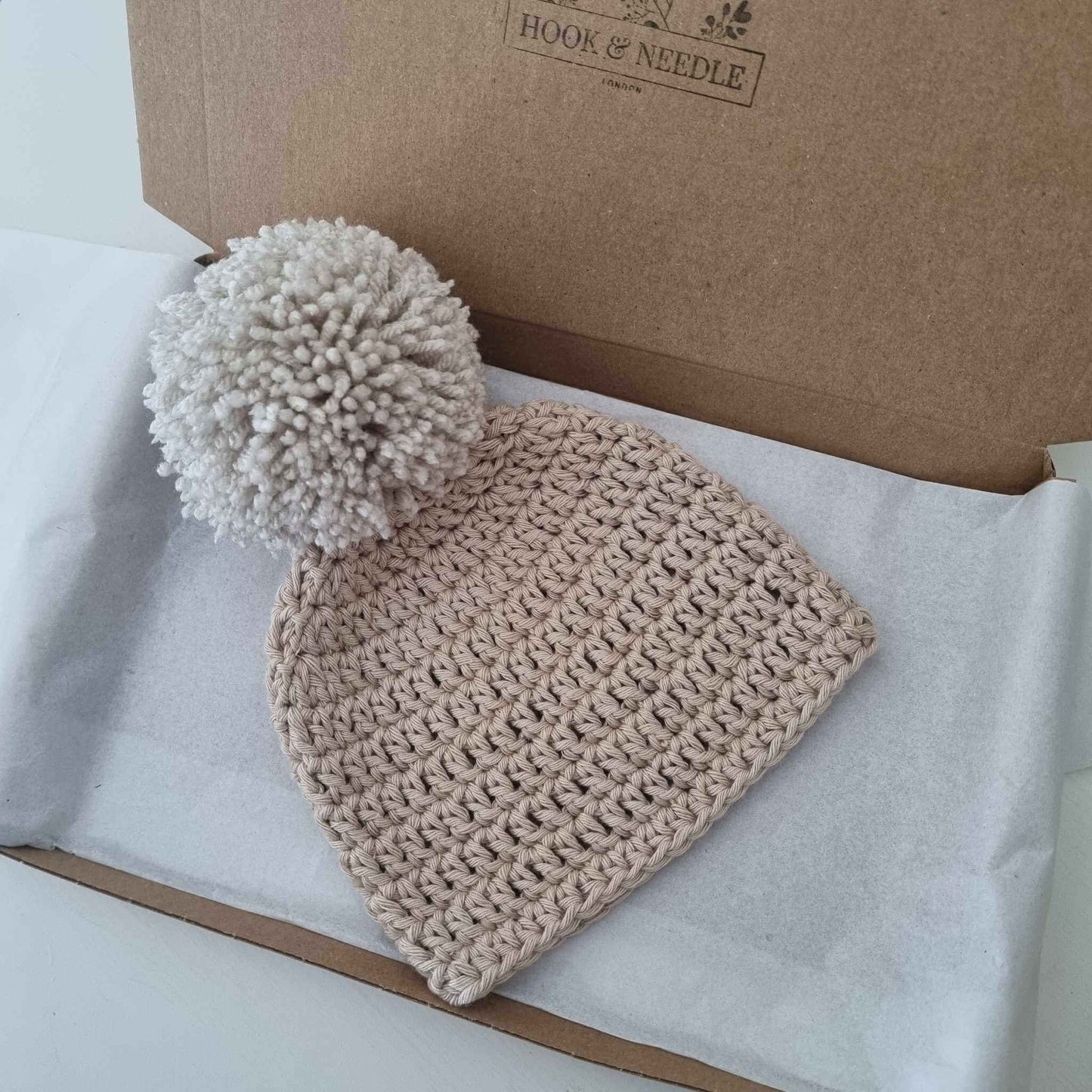  A delightful stone coloured crochet hat with a cheerful pom pom, perfect for staying warm while looking fashionable in winter.