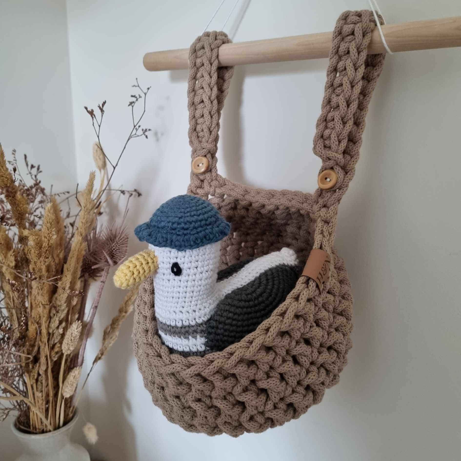 An adorable handmade cot basket is hanging from a wooden dowel with a cuddly toy inside.