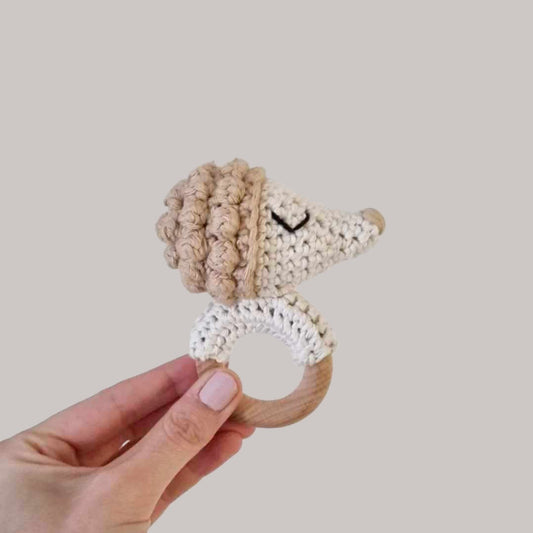 A hand showcases a delightful crocheted hedgehog rattle, emphasizing its playful design for babies.