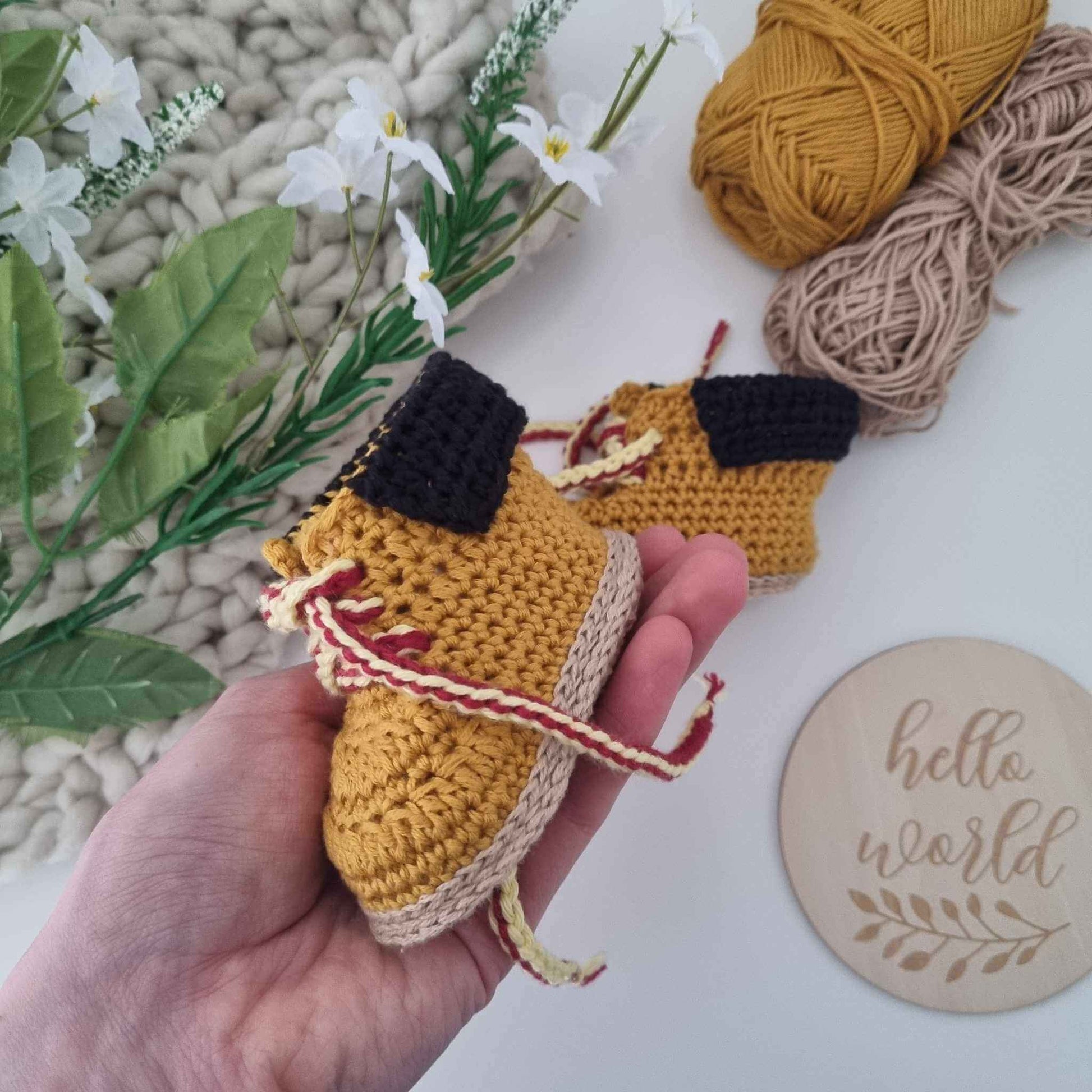 A hand holding a delightful pair of crocheted baby shoes paired with a soft yarn ball, ideal for cozying up tiny toes in style.