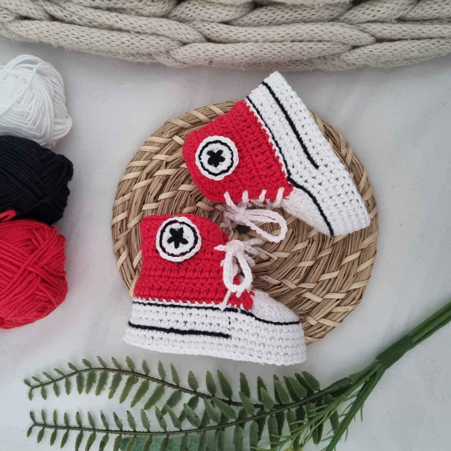 A delightful pair of red crocheted baby shoes paired with a soft yarn ball, ideal for cozying up tiny toes in style.