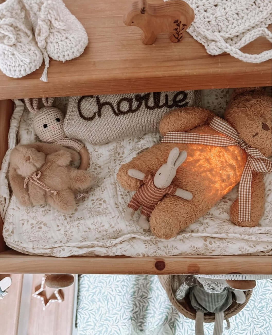 Crochet Bunny Rattle among soft toys and accessories in a wooden drawer, creating a cozy baby environment.