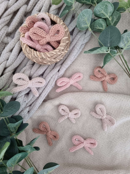 Handmade crochet bow hair clips in soft pastel colors displayed with greenery, perfect for little outfits.