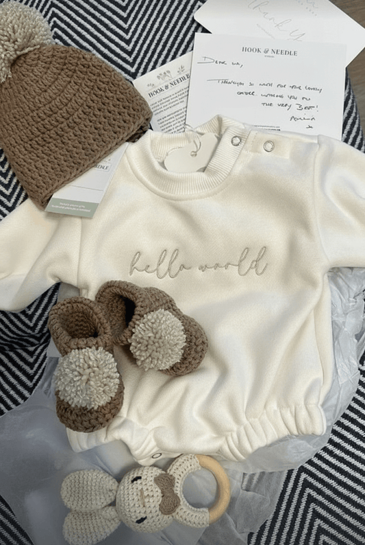 Baby Hat & Boots Set - Brown Pom Pom featuring a crocheted brown hat, matching boots, and a cozy outfit.