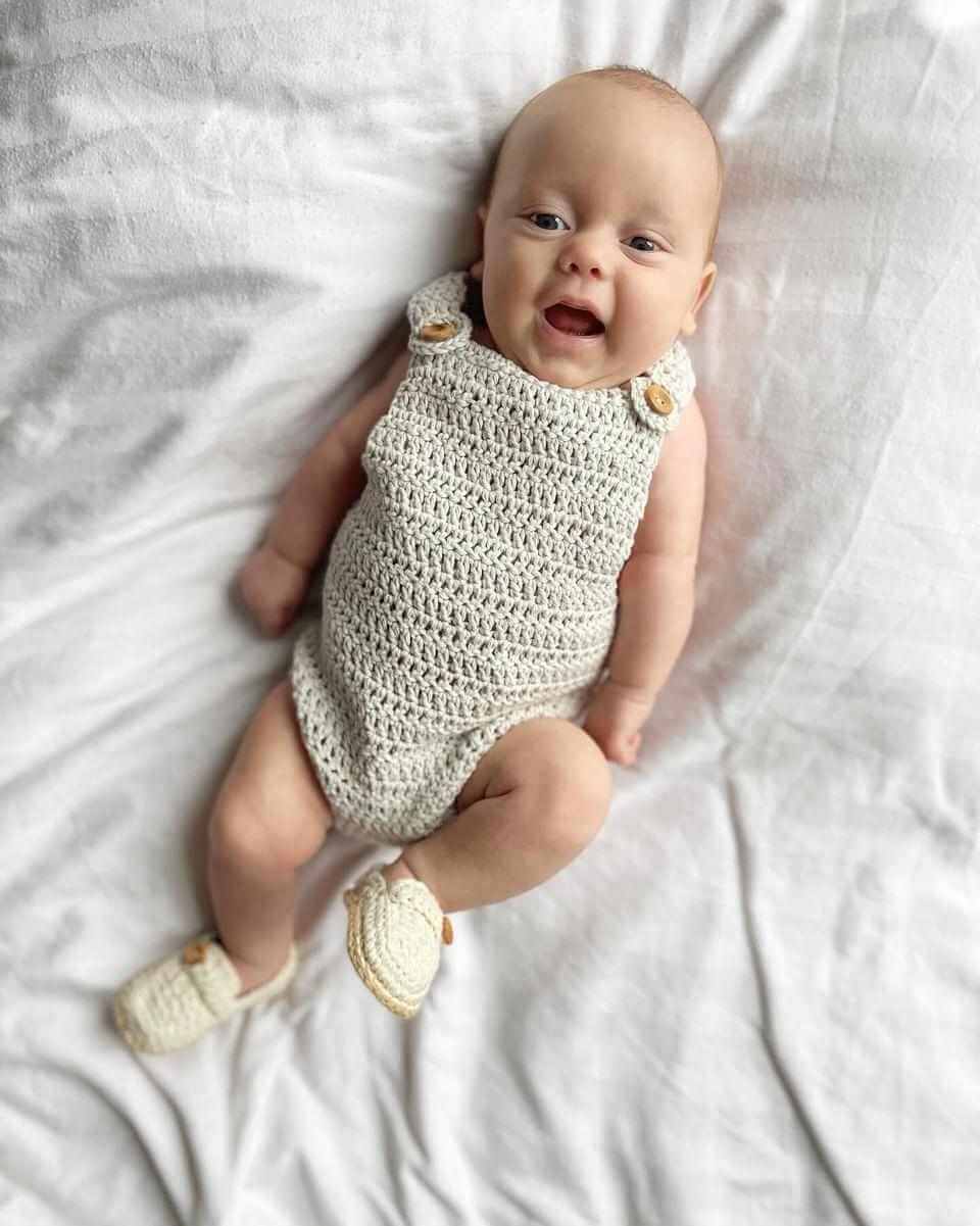 A baby in a cozy crocheted romper peacefully lying on a soft bed, radiating cuteness and comfort.