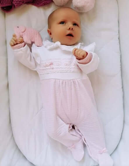 A baby hold a soft, pink elephant rattle