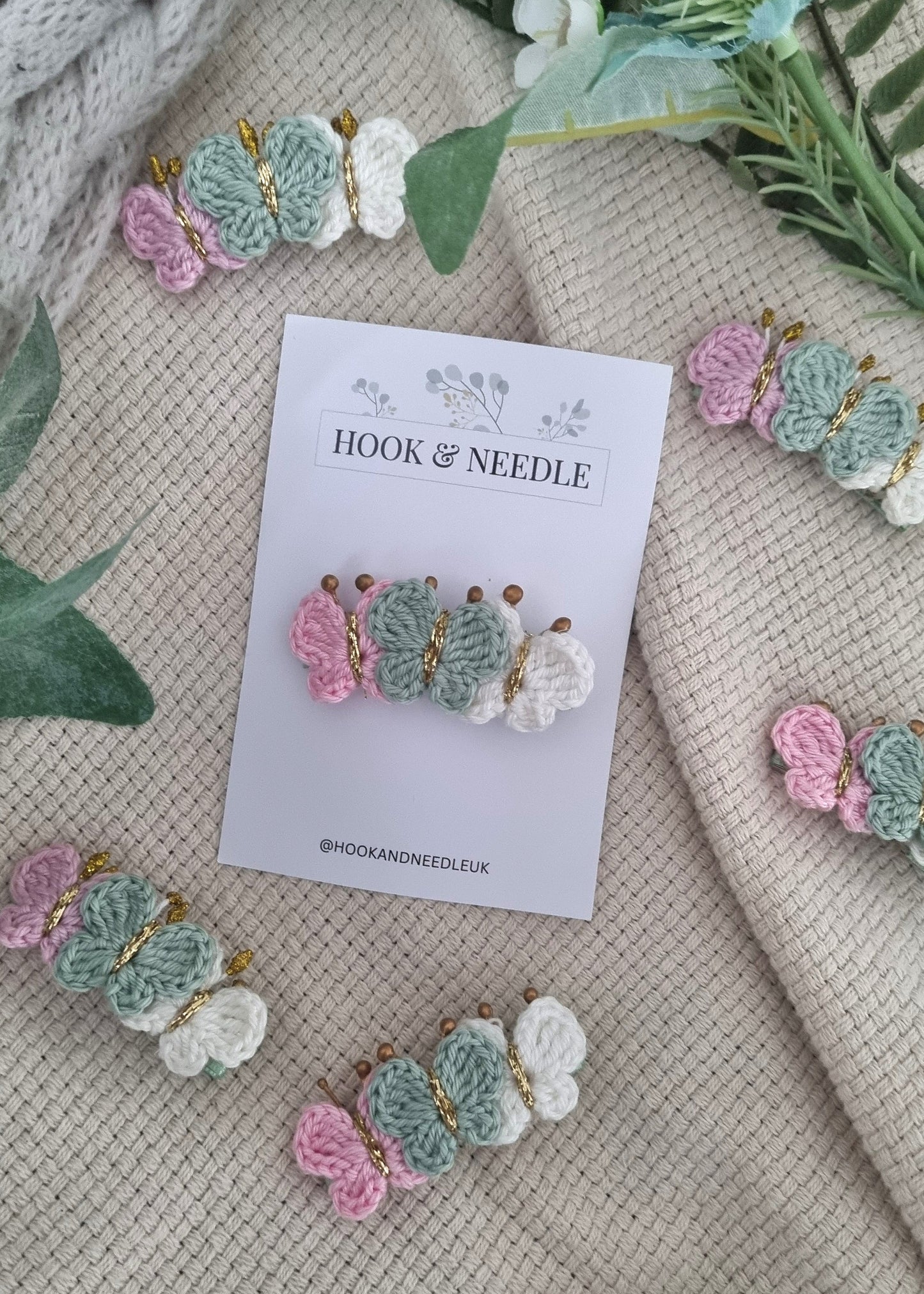 Butterfly-shaped hair clips on a beige fabric background with 'Hook & Needle' branding.