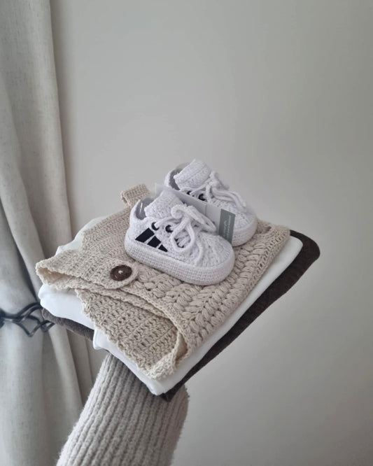 White baby shoes on a folded beige blanket against a neutral background