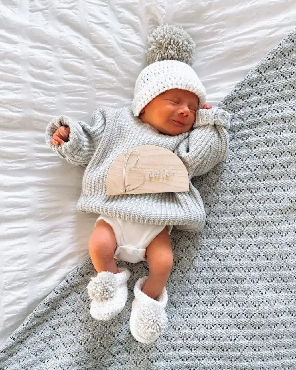 Baby wearing a cotton hat and boot set in white with pom pom detail