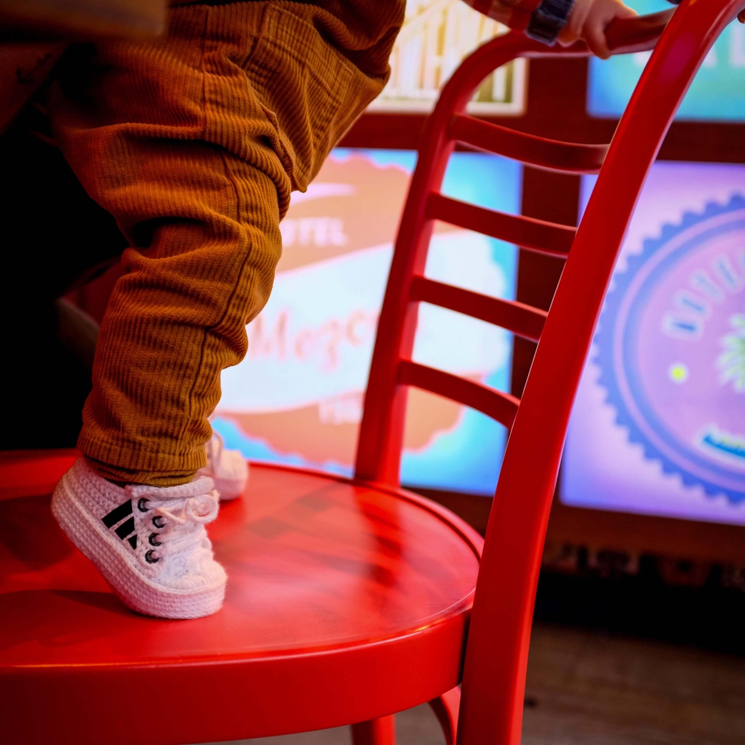 Child sitting on a red chair with a colorful screen in the background