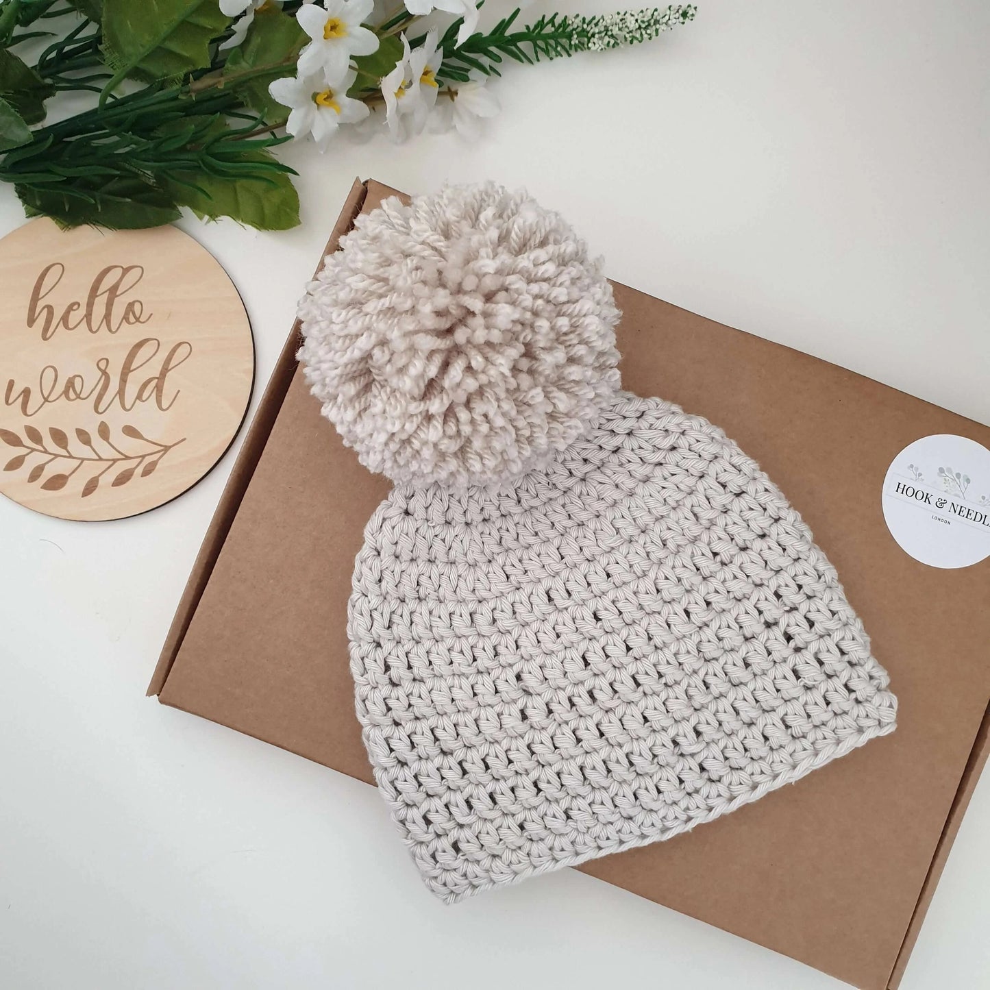 A charming oatmeal crochet hat adorned with a fluffy pom pom, ideal for adding a touch of fun to any winter outfit.