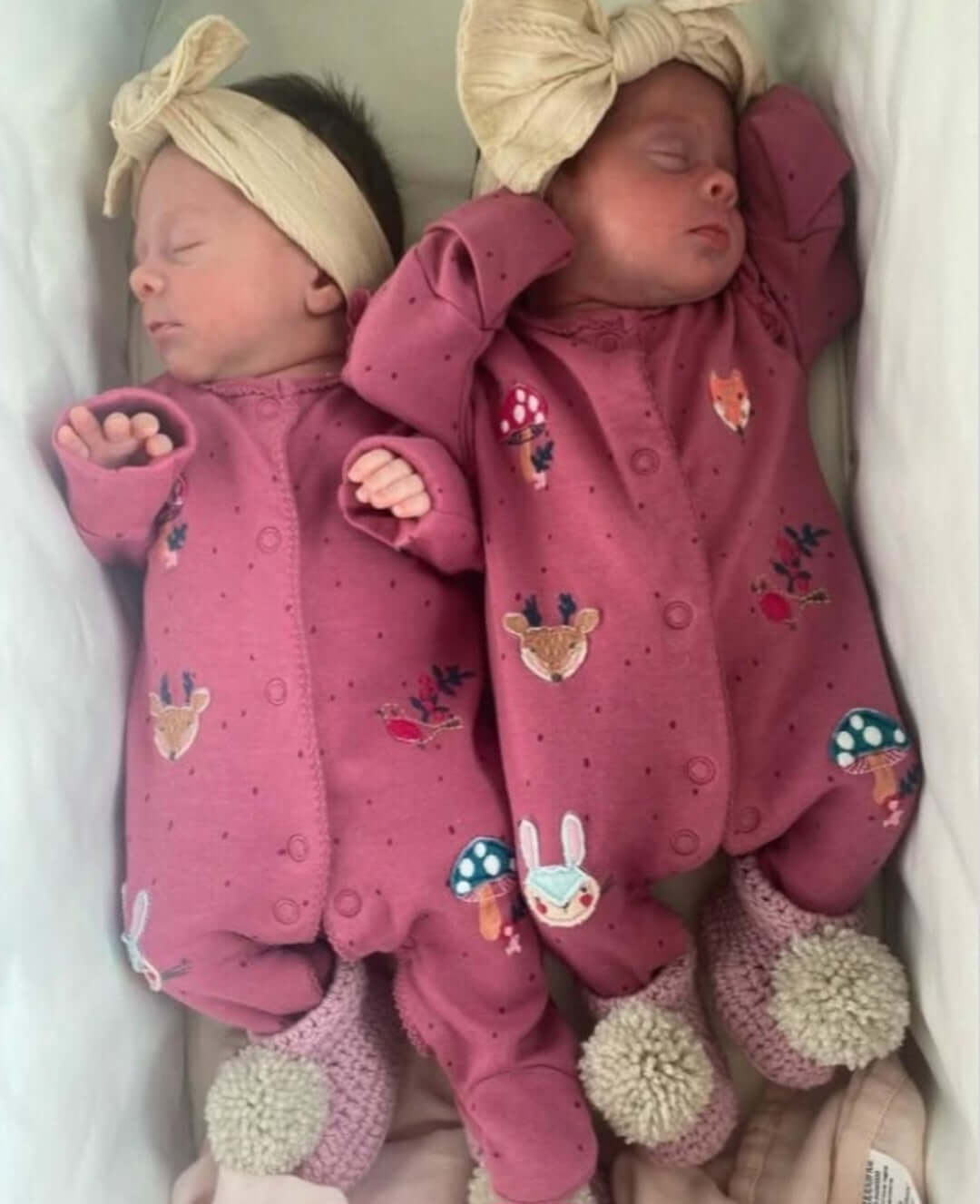 Two newborn babies in pink outfits with floral patterns, lying side by side.