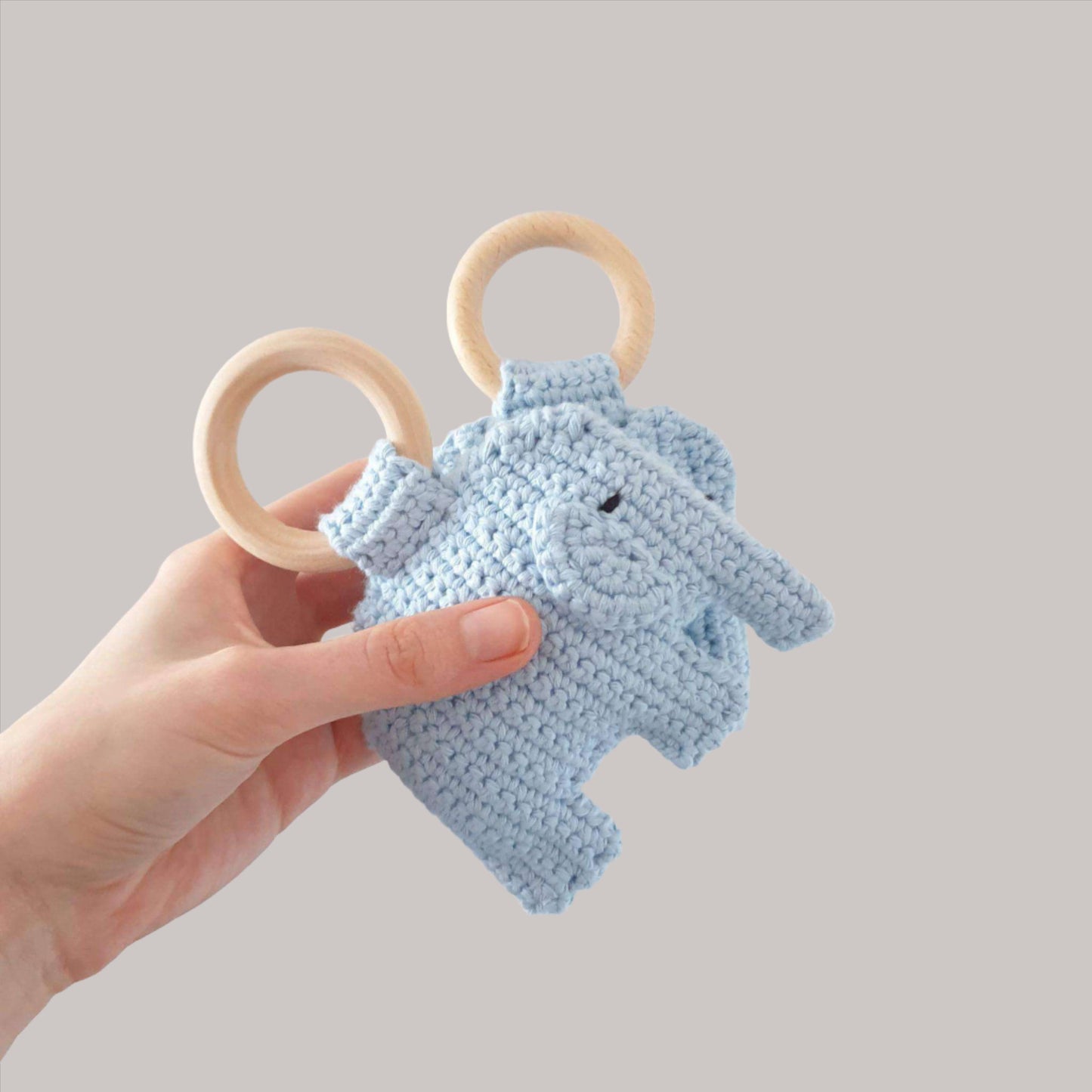 A hand holds a soft, blue crocheted elephant rattle, showcasing its cute design and wonderful colour.