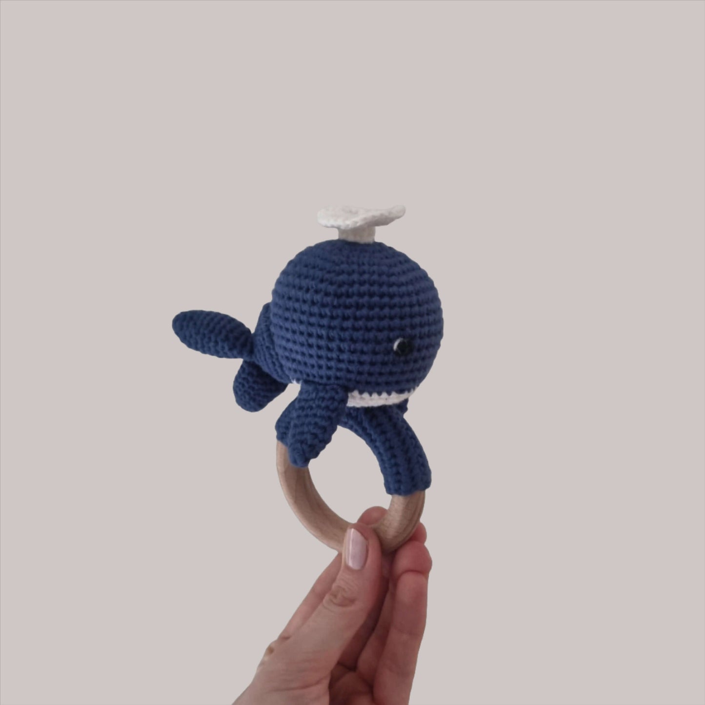  A hand presents a charming crocheted whale rattle, highlighting its adorable features and handmade quality.