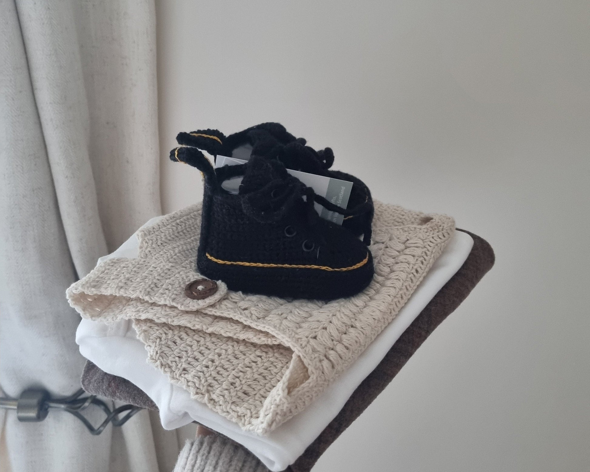 Black baby shoe on a folded beige blanket against a neutral curtain background