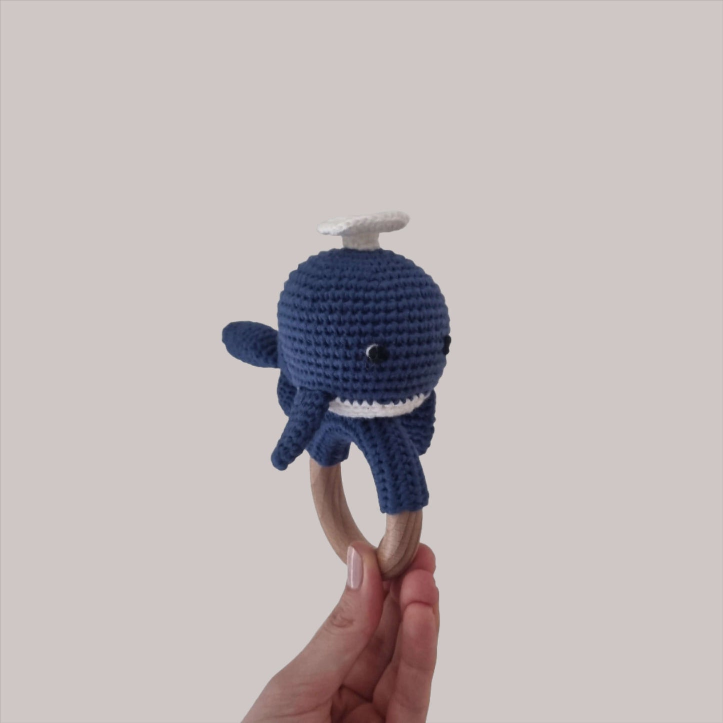 A hand gently holds a dark blue crocheted whale rattle, perfect for little ones to enjoy and play with.