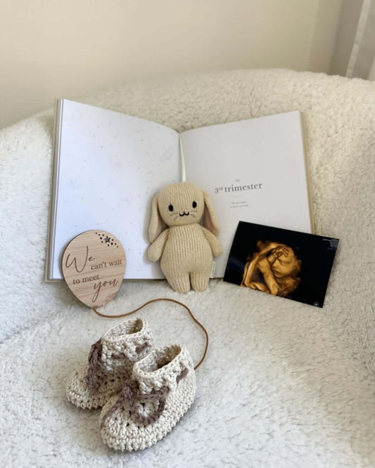 Cotton baby boots - Brown/Cream placed alongside a stuffed bunny, ultrasound photo, and a pregnancy book.