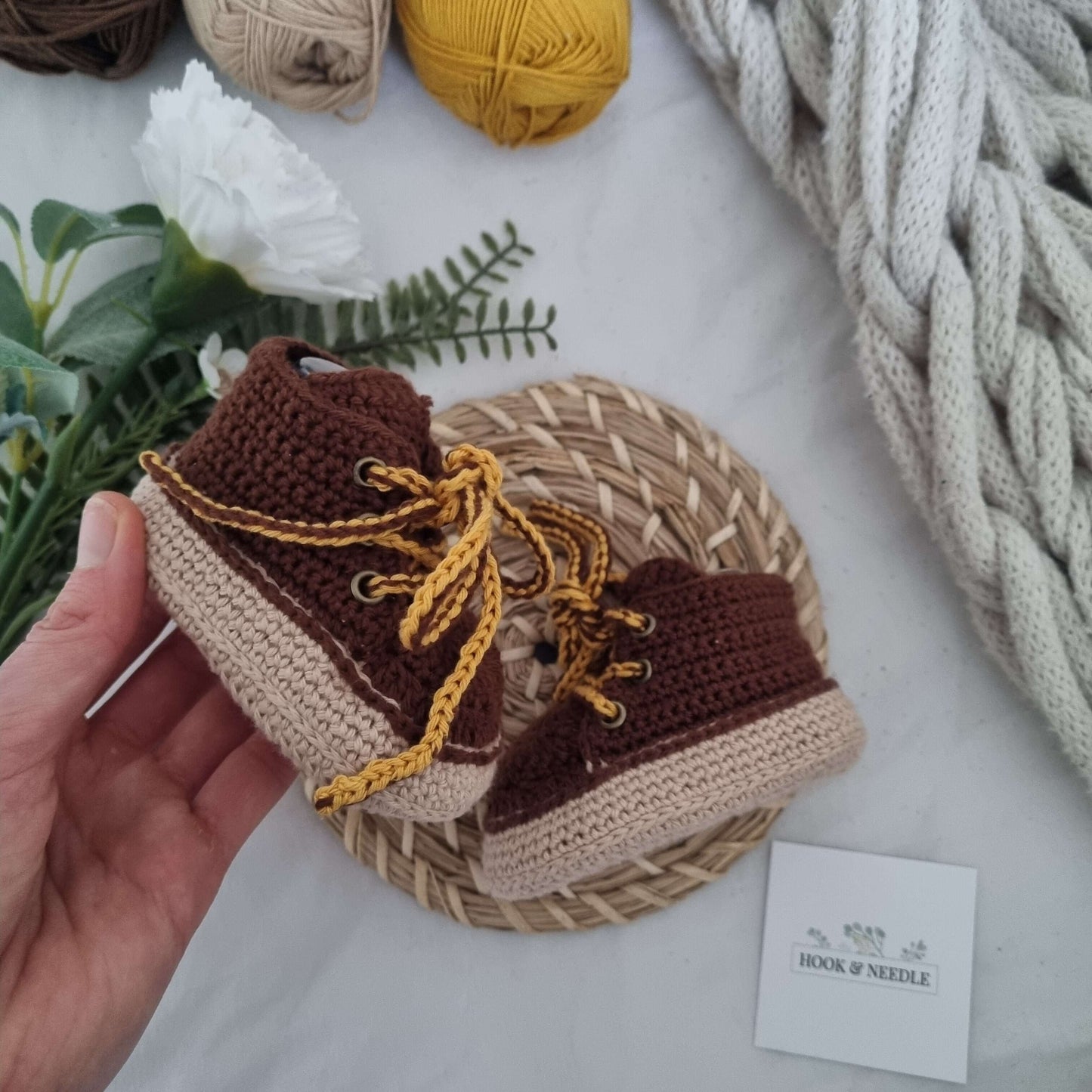 Crochet baby boots with lace-up design, hand-crocheted in brown and beige, displayed on a woven mat.