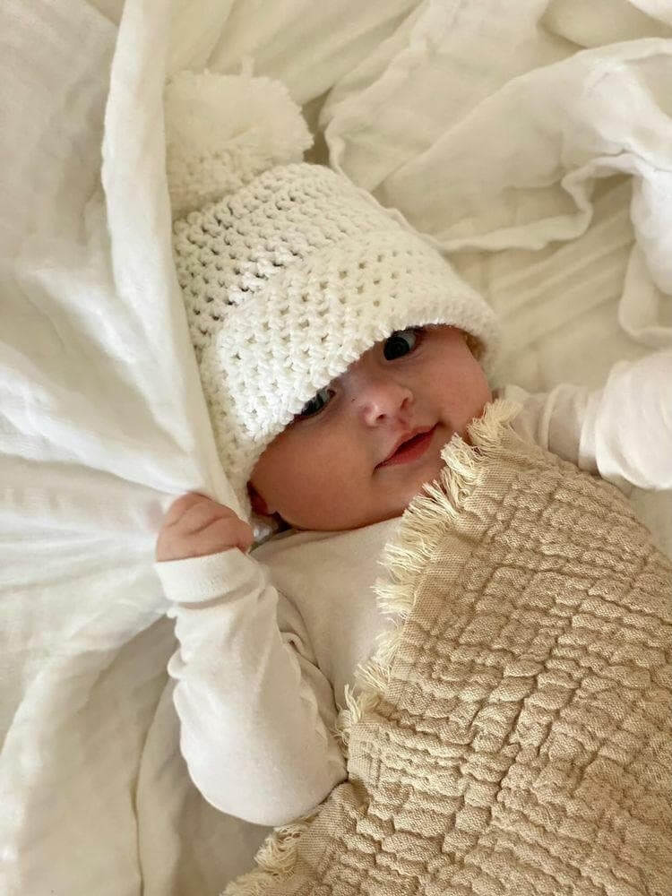 Baby wearing acrylic pom pom hat in white